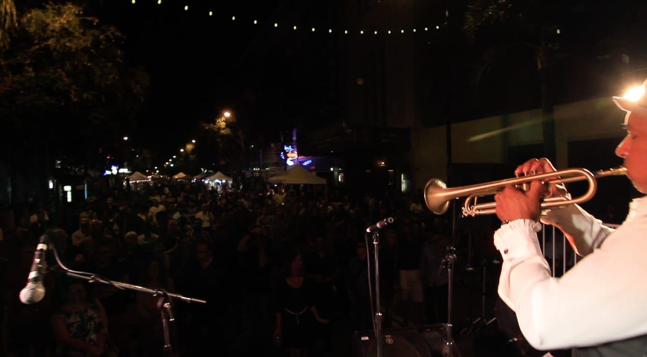 Doug Ellington playing trumpet in profile before a night crowd under string lights
